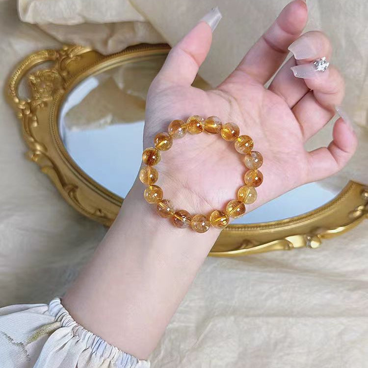 Hand wearing a amber beaded bracelet with a gold-framed mirror in the background