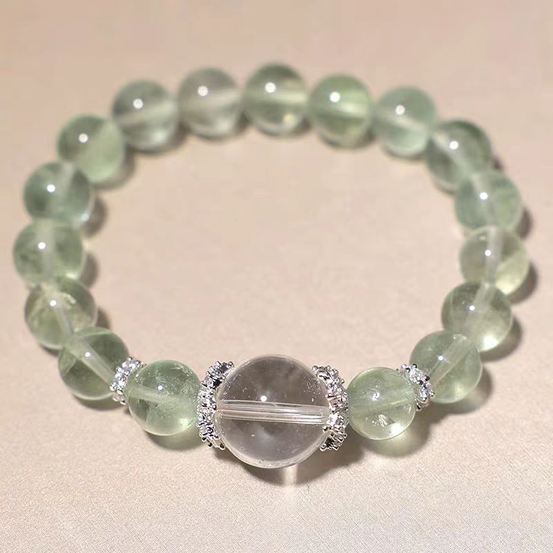 Green beaded bracelet with a clear crystal bead on a beige background