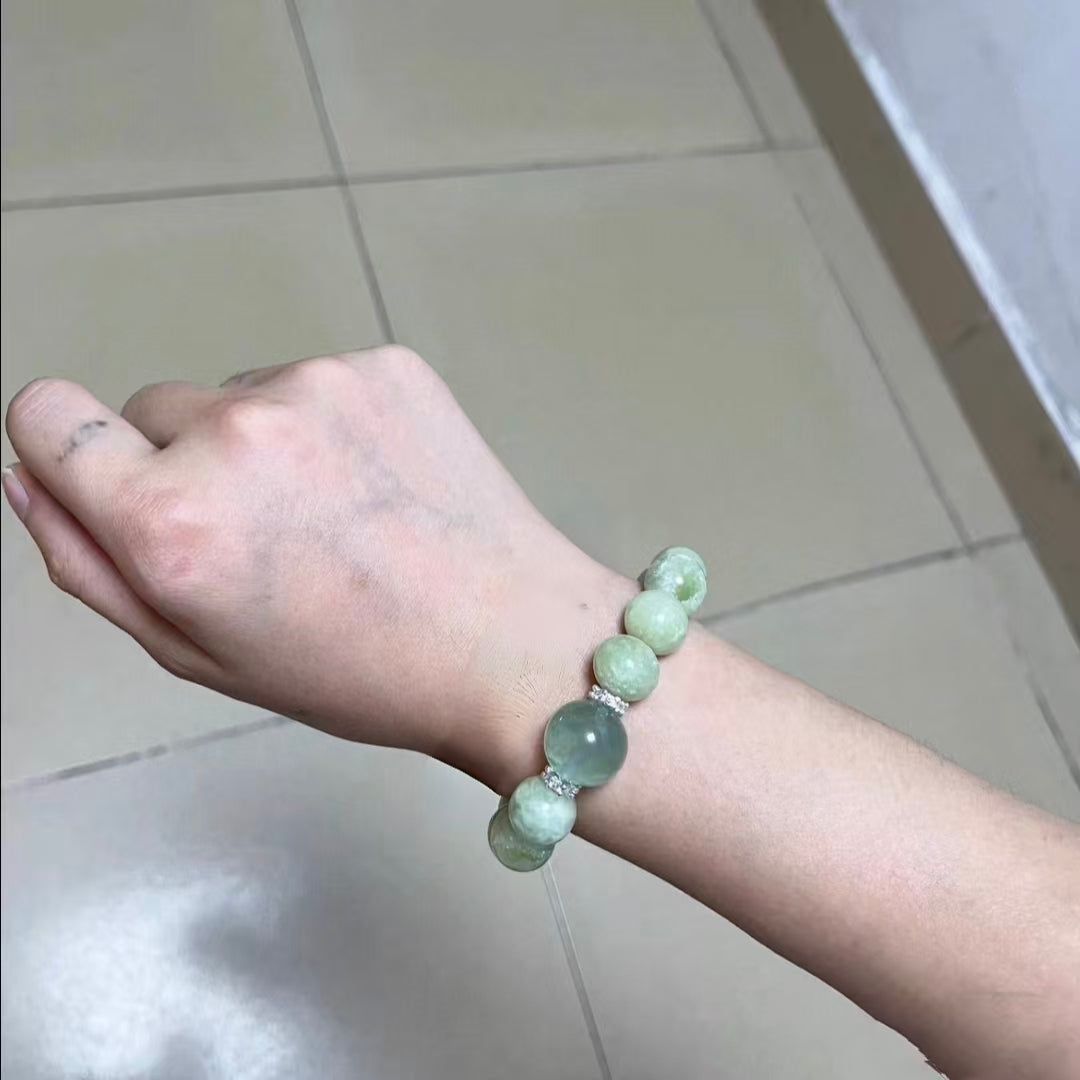 Hand wearing a bracelet with green beads on a tiled floor background
