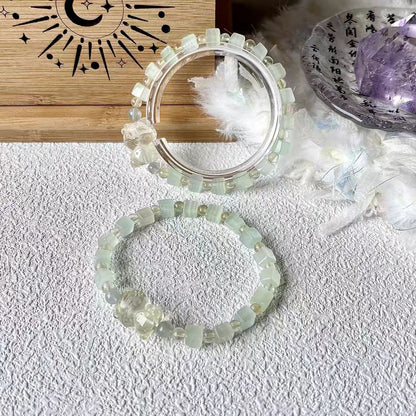Two beaded bracelets on a textured surface with a wooden board and decorative items in the background.