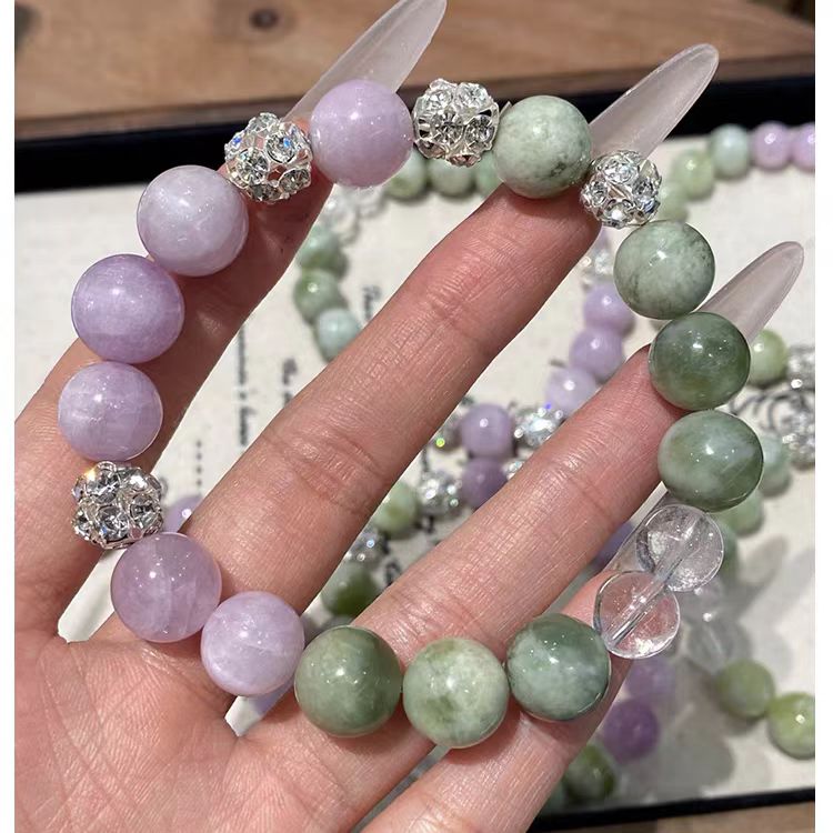 Hand holding a bracelet with green and purple beads and silver accents.