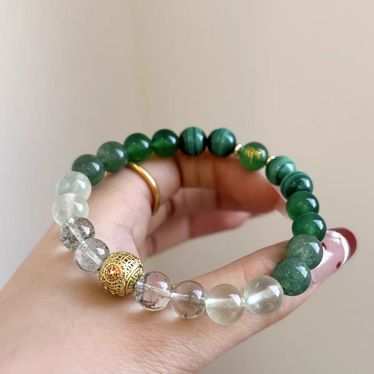 Beaded bracelet with green, clear, and gold beads on a hand against a plain background