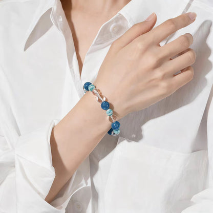 Hand wearing a bracelet with blue beads against a white shirt background
