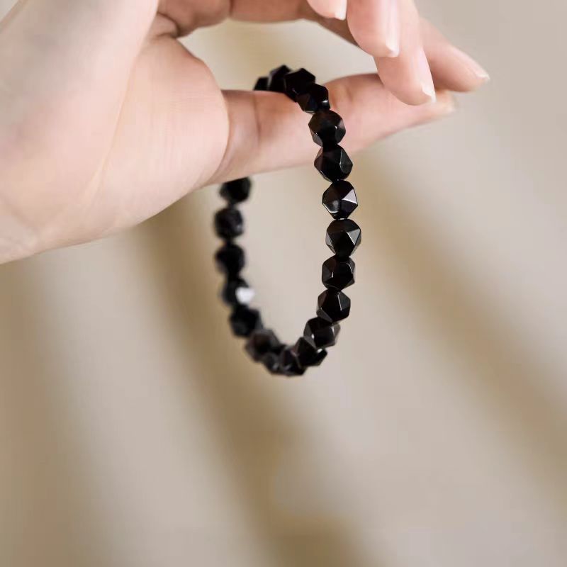 Black beaded bracelet held by a hand against a neutral background