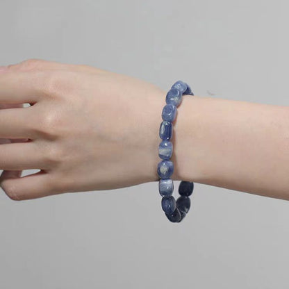 Hand wearing a blue beaded bracelet on a plain background