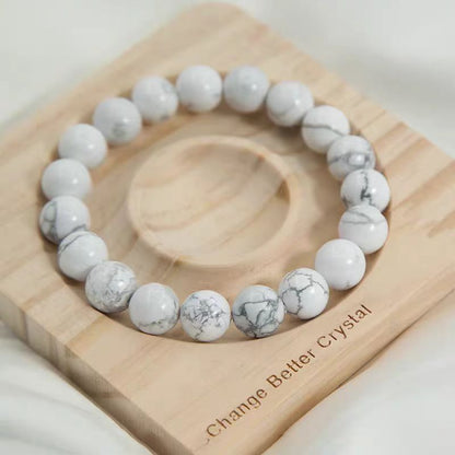 White beaded bracelet on a wooden block with 'Change Better Crystal' text