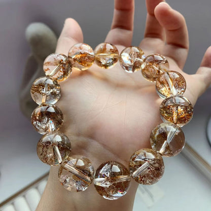 Hand holding a bracelet with brown and clear beads against a neutral background