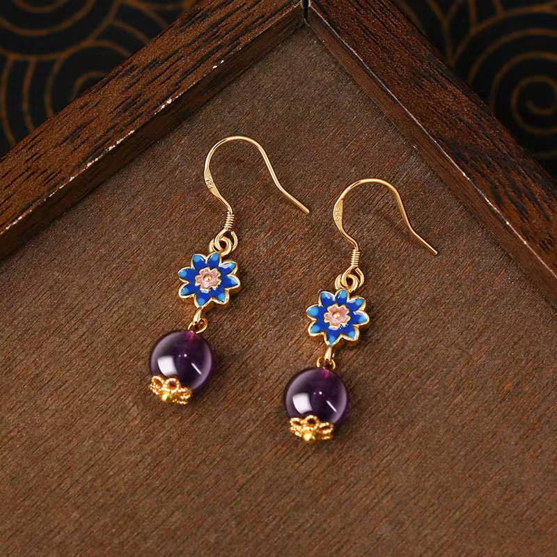 Pair of gold earrings with blue flower designs and purple beads on a wooden surface.