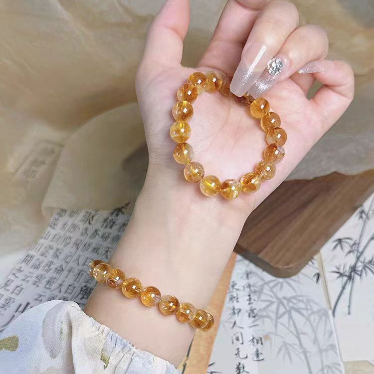 Hand wearing a yellow beaded bracelet on a light background