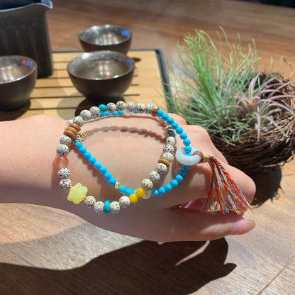 Hand wearing a stack of colorful beaded bracelets on a wooden surface with a plant in the background.