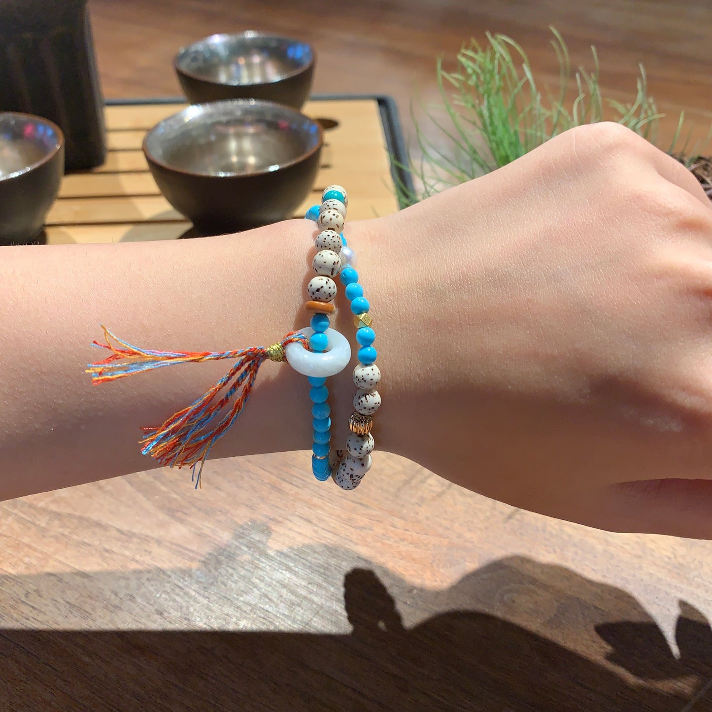 Hand wearing a colorful bracelet with beads and tassels on a wooden surface