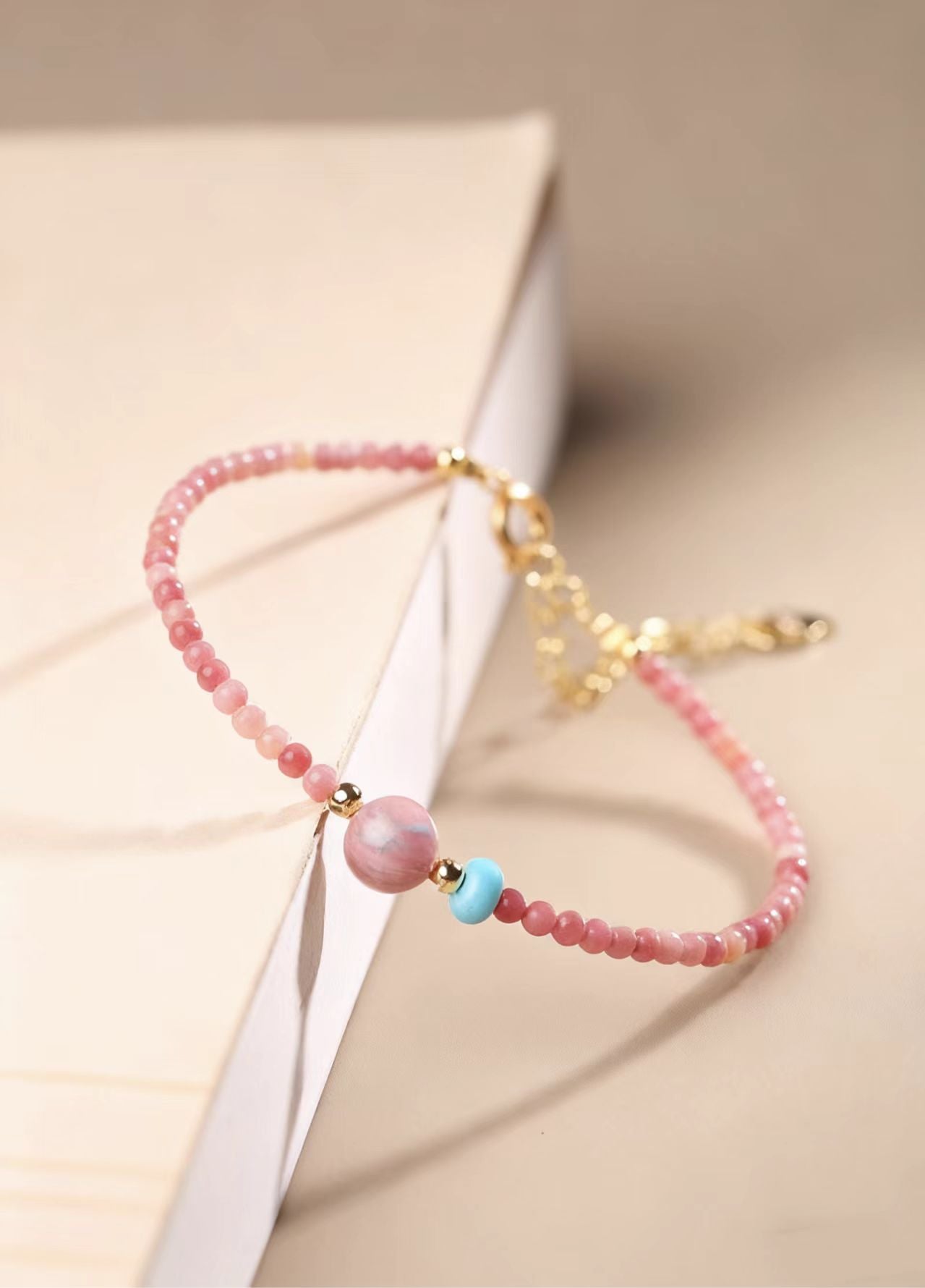 Beaded bracelet with pink and gold elements on a beige background