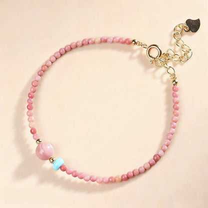 Pink beaded bracelet with a gold clasp on a beige background